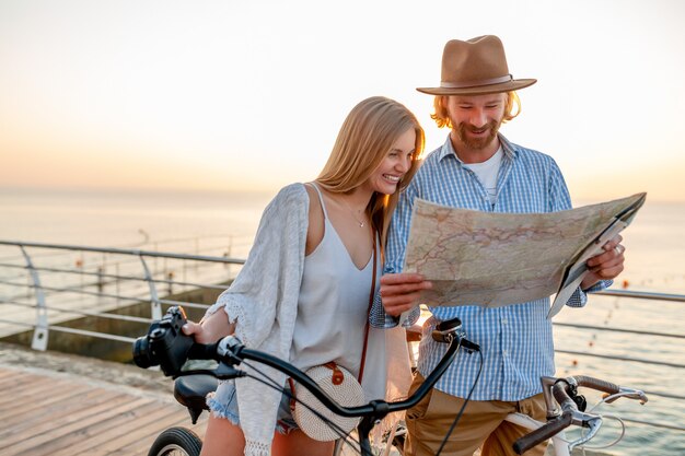 Attrayant couple heureux d'amis voyageant en été sur des vélos, homme et femme aux cheveux blonds mode style hipster boho s'amusant ensemble