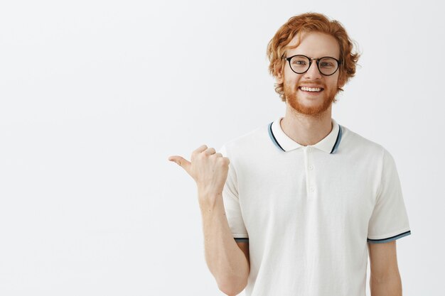 Attrayant mec rousse barbu posant contre le mur blanc avec des lunettes