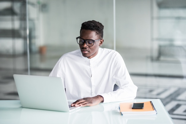 Attrayant travailleur travailleur de bureau positif jeune assis au bureau en face de l'ordinateur portable ouvert