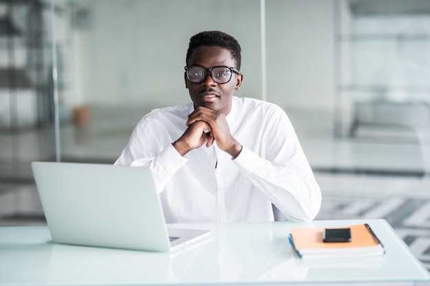 Attrayant travailleur travailleur de bureau positif jeune assis au bureau en face de l'ordinateur portable ouvert