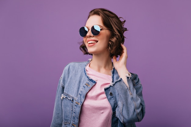 Attrayante jeune femme à lunettes de soleil scintillantes à la recherche de distance Portrait de modèle européen glamour avec coupe de cheveux courte souriant.