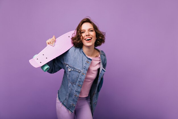 Attrayante jeune femme en tenue décontractée souriant. Belle fille européenne avec planche à roulettes s'amuser.