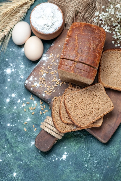 Photo gratuite au-dessus des blés de pain noir diététiques sur des pointes de planche de bois farine d'oeufs de fleur dans un bol sur fond bleu