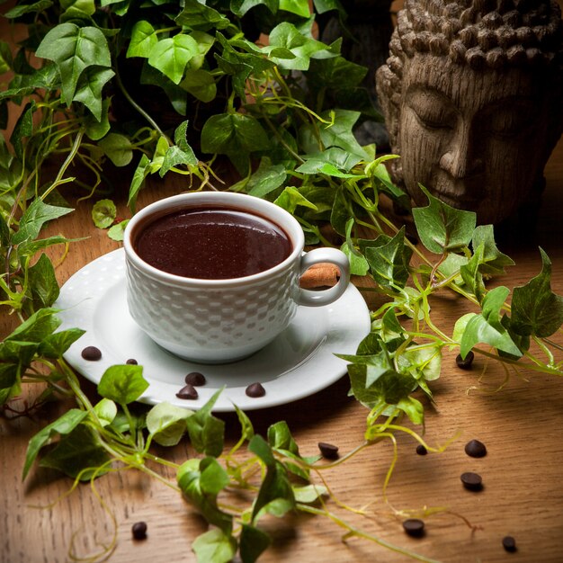 Au-dessus du café turc avec des grains de café et une branche de raisin et une tête de statue dans une tasse