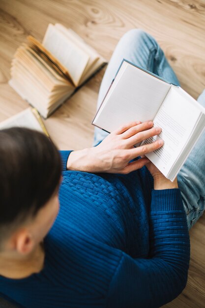 D&#39;au-dessus de l&#39;homme appréciant la lecture sur le plancher en bois