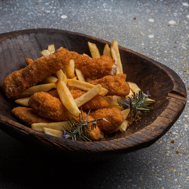 Au-dessus de pépites de poulet avec des frites dans une assiette en bois