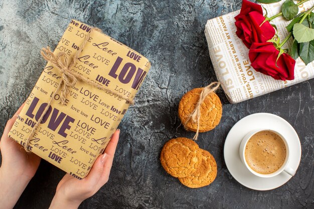 Au-dessus de la vue de beaux coffrets cadeaux roses rouges biscuits empilés une tasse de café sur fond sombre glacial