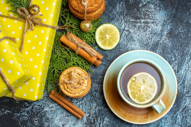 Au-dessus De La Vue De Fond De Noël Avec De Belles Boîtes-cadeaux Jaunes Et Des Biscuits Empilés Citron Cannelle Limes à Côté D'une Tasse De Thé Noir Sur Fond Sombre