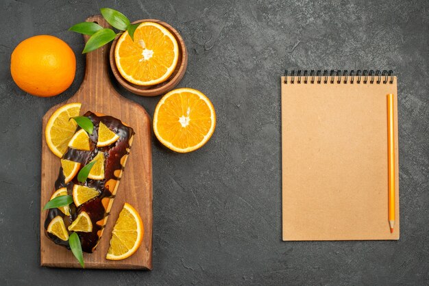 Au-dessus de la vue de savoureux gâteaux entiers et coupés des oranges sur une planche à découper à côté de l'ordinateur portable sur le tableau noir