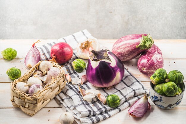 Aubergines; choux de Bruxelles; oignon; gousses d&#39;ail et chiffon sur table en bois