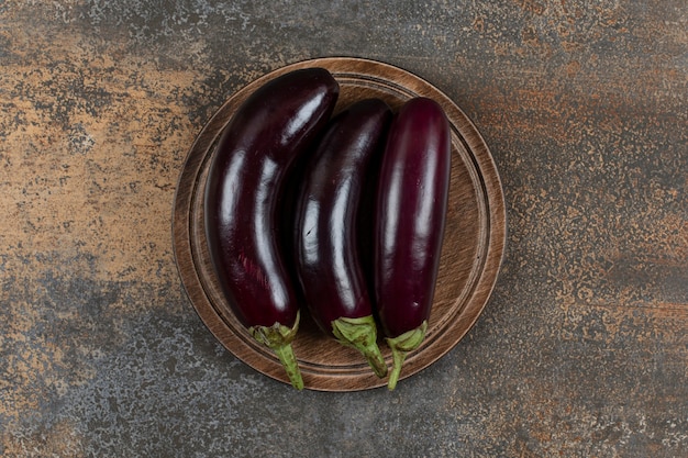 Aubergines crues fraîches au tableau sur la surface en marbre