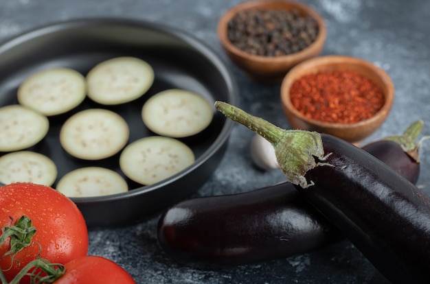 Aubergines crues tranchées dans une poêle avec des tomates et des épices.