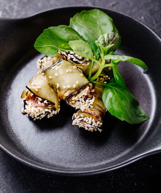 Aubergines roule avec des feuilles basiliques à l'intérieur du pan noir.