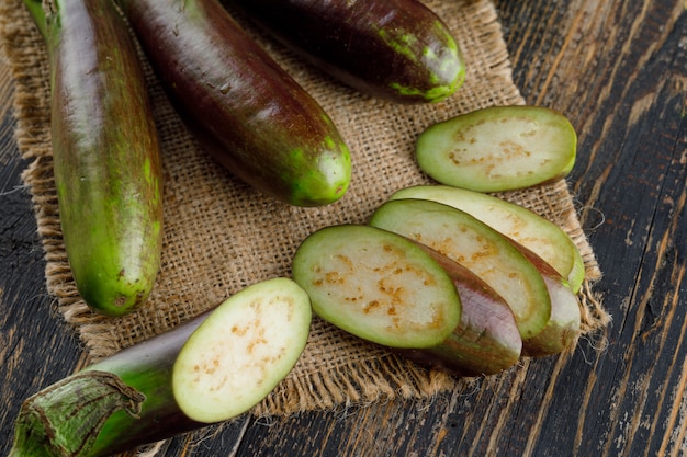 Aubergines avec tranches sur bois et morceau de sac, gros plan.