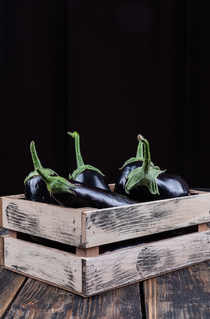 Aubergines vue latérale dans une boîte en bois sur fond en bois et noir. espace vertical pour le texte