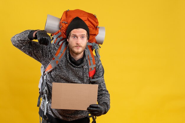 auto-stoppeur masculin avec des gants en cuir et un sac à dos tenant un carton vierge pointant vers le sol