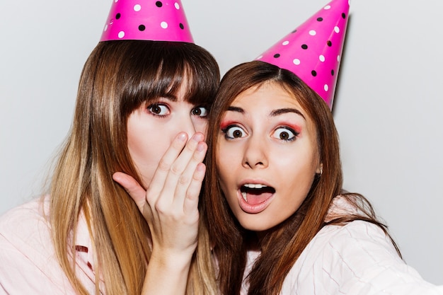 Autoportrait de deux femmes en chapeaux d'anniversaire en papier rose. Amis portant un pyjama rose