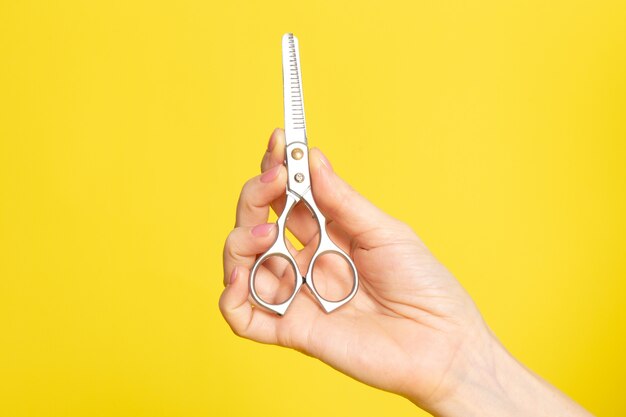 Un avant fermé vue argent ciseaux à cheveux sur la main de la femme sur la couleur de fond jaune les cheveux du corps