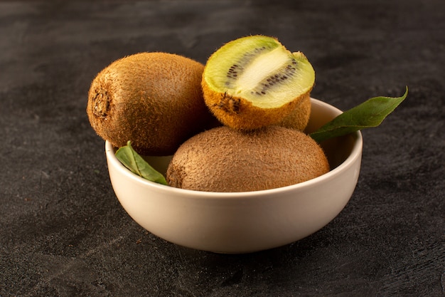 Photo gratuite un avant fermé vue kiwis bruns mûrs frais isolés juteux et fruits entiers avec des feuilles vertes à l'intérieur de la plaque blanche