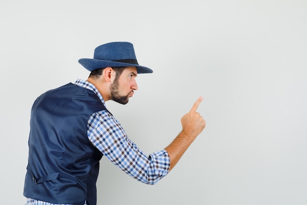 Avertissement de jeune homme avec le doigt en chemise, gilet, chapeau et à la rage. .