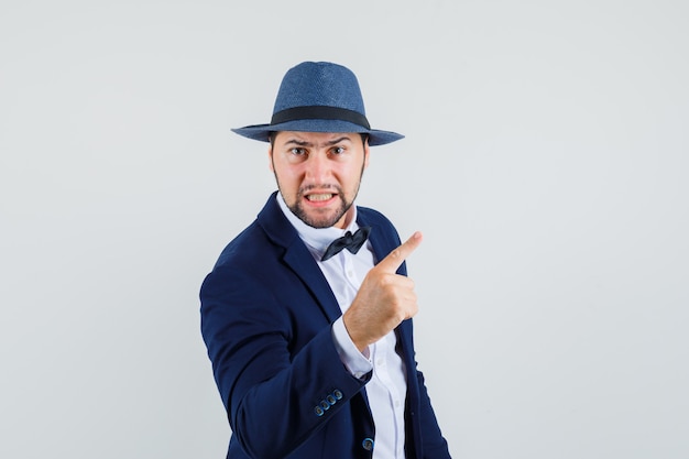 Avertissement de jeune homme avec le doigt en costume, chapeau et l'air nerveux. vue de face.