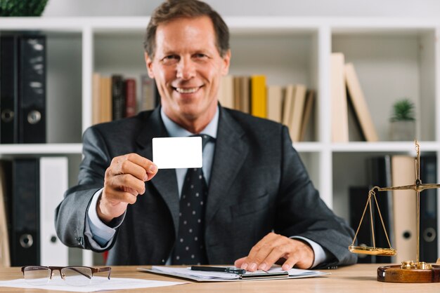 Avocat mature souriante montrant une carte de visite vide assis dans la salle d&#39;audience