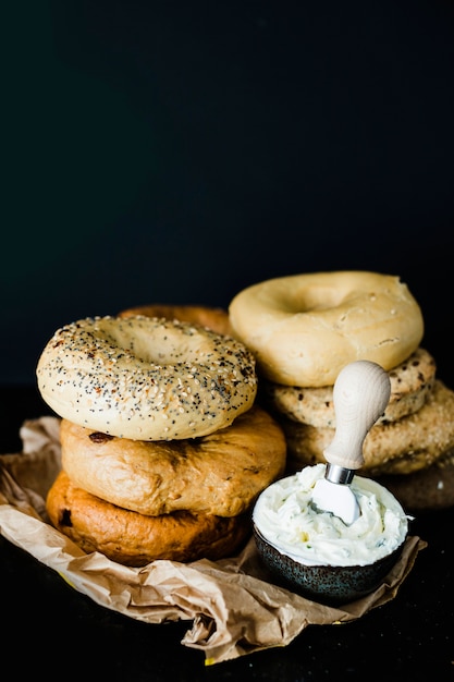 Bagel empilé de différents types de bagels avec du fromage dans le bol sur fond noir