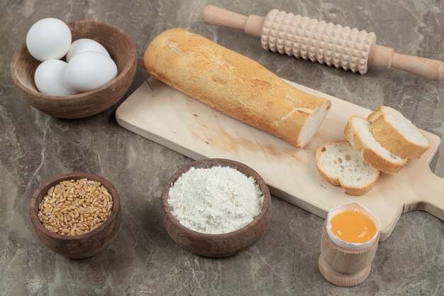 Baguette, œufs, farine, orge et rouleau à pâtisserie sur une surface en marbre. Photo de haute qualité