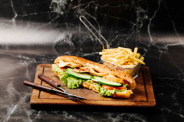 Baguette sandwich avec des ingrédients mélangés et des frites sur une planche de bois.