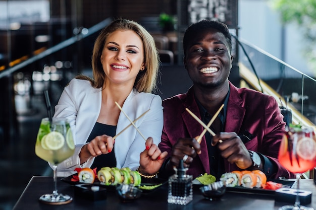 Photo gratuite baguettes croisées. deux jeunes amis heureux mangent ensemble des rouleaux de sushi au café.