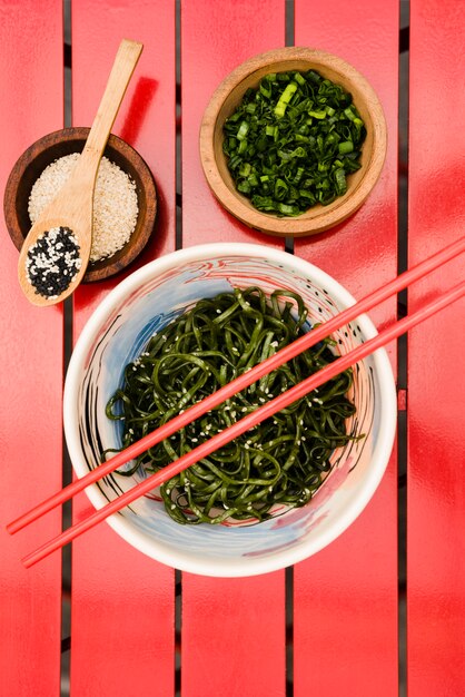 Des baguettes sur la salade d&#39;algues chuka japonaise servie avec des graines de sésame et des oignons nouveaux hachés sur une table rouge