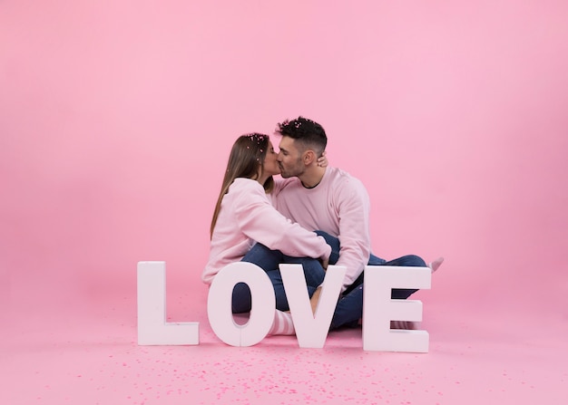 Baiser de jeune couple près de grand signe d&#39;amour et de confettis