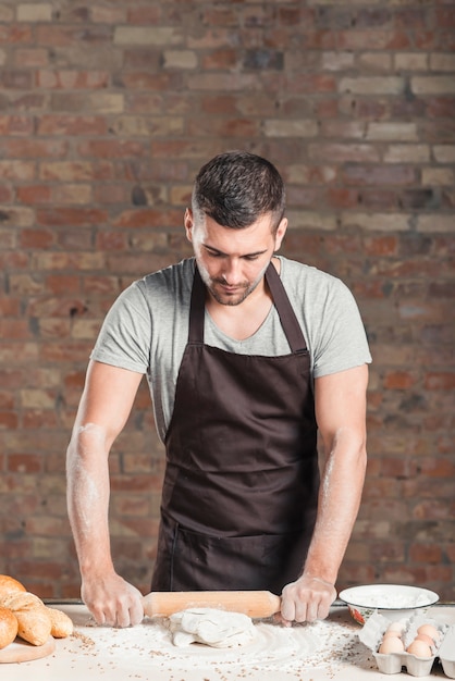 Baker en appuyant sur la pâte avec rouleau à pâtisserie sur le comptoir de la cuisine