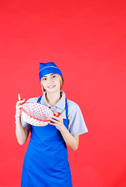 Baker femelle en tablier bleu tenant une corbeille à pain avec une serviette rouge à l'intérieur