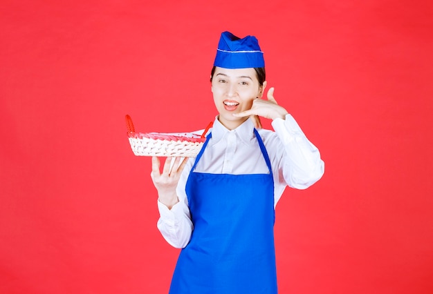 Baker En Tablier Bleu Tenant Une Corbeille à Pain Avec Une Serviette Rouge à L'intérieur Et Demandant D'appeler Et De Commander.