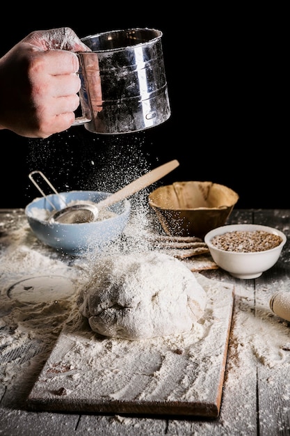 Baker tamisant la farine à travers un tamis sur une table en bois