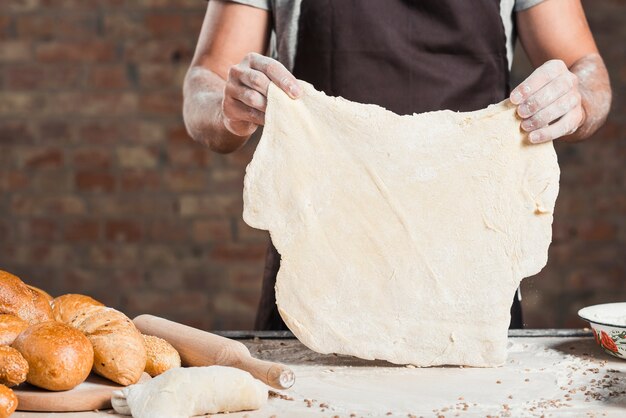 Baker tenant une pâte aplatie sur un comptoir de cuisine