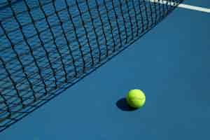 Photo gratuite la balle de tennis jaune est posée près du filet noir du court de tennis ouvert.