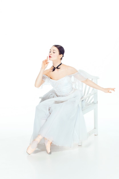 Ballerine en robe blanche assise sur une chaise blanche, studio blanc.