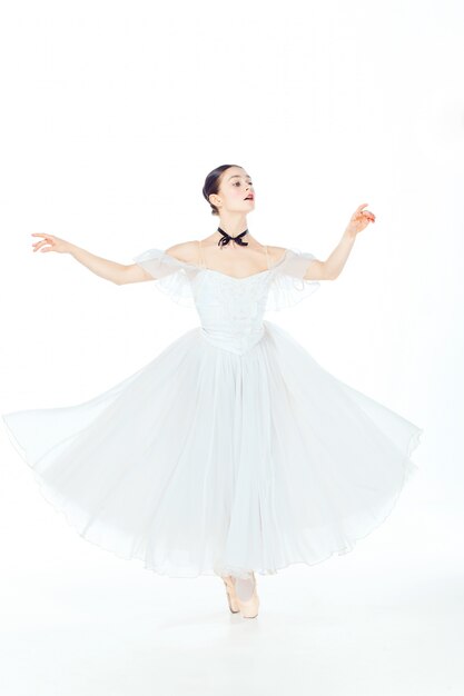 Ballerine en robe blanche posant sur des pointes, fond de studio.