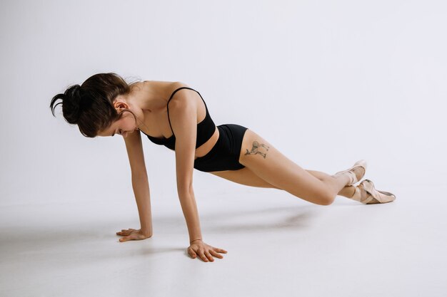 Ballet de mode. Jeune danseuse de ballet en body noir sur fond blanc. Ballerine caucasienne comme un mannequin.