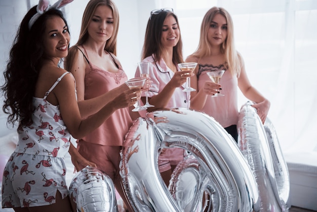 Avec des ballons de couleur champagne et argent sur la fête. Quatre jolies filles sympas ont un week-end