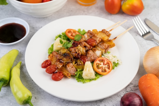 Barbecue avec une variété de viandes, avec tomates et poivrons sur une plaque blanche.