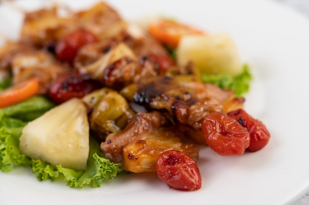 Barbecue avec une variété de viandes, avec tomates et poivrons sur une plaque blanche.