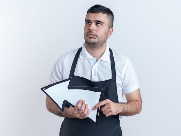 Barber man in apron holding arrow jusqu'à perplexe debout sur fond blanc