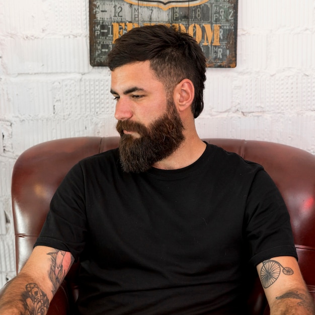 Barbier barbu assis sur une chaise au salon de coiffure