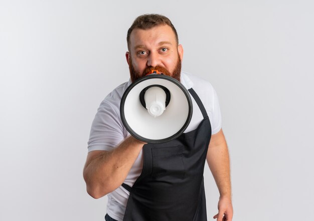 Barbier barbu professionnel en tablier criant au mégaphone debout sur un mur blanc