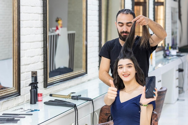 Le barbier étirant les cheveux de son client et le geste du client pouce vers le haut Photo de haute qualité