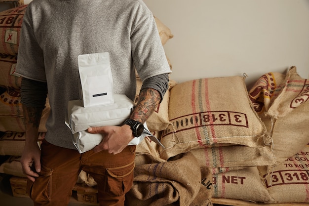 Photo gratuite barista tatoué détient des sacs d'emballage vierges avec des grains de café fraîchement cuits prêts pour la vente et la livraison