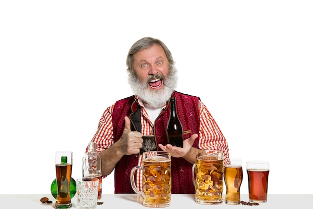 Photo gratuite le barman masculin expert senior avec de la bière au studio isolé sur un mur blanc